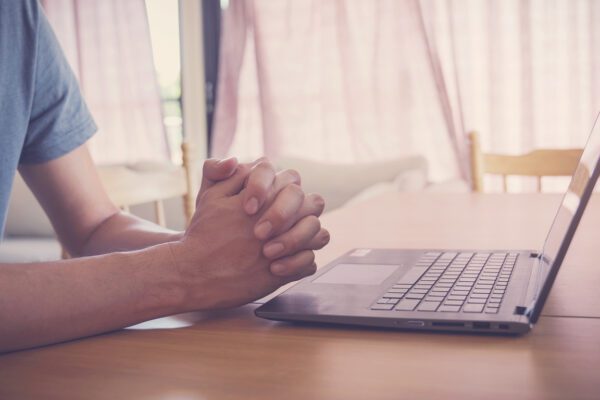 Praying hands with laptop, worship online at home, streaming online to demonstrate church live stream setup